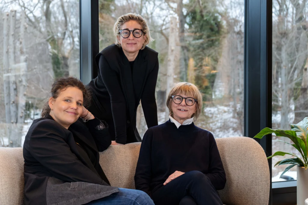 Tre personer opholder sig i et loungeområde, de sidder og står omkring en sofa som led i et space management & design‑arbejde.