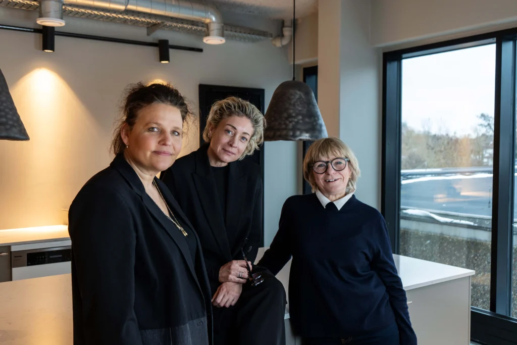 Tre personer står i et moderne køkken- og loungeområde og drøfter ideer inden for space management & design.