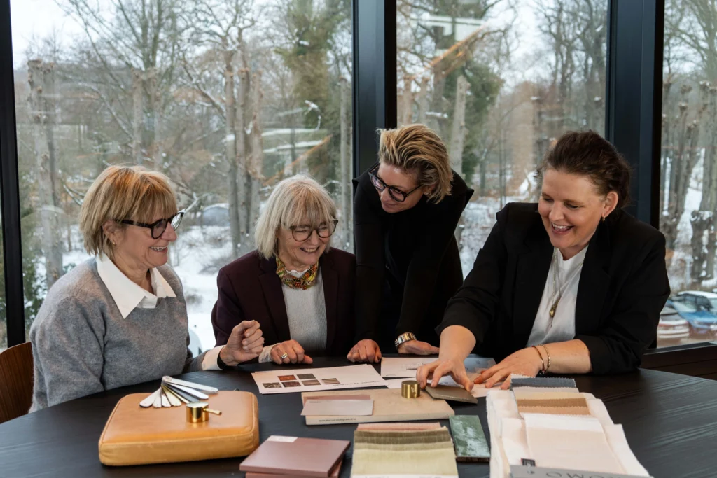 En gruppe personer arbejder sammen om space management & design ved et bord fyldt med materialeprøver, farvekort og skitser.