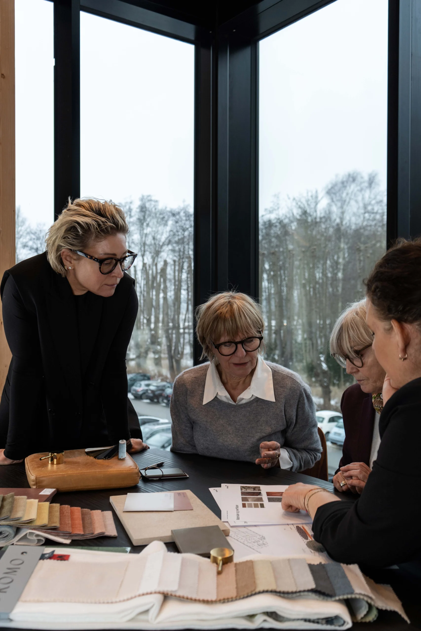 En gruppe personer arbejder sammen om space management & design ved et bord fyldt med materialeprøver, farvekort og skitser.